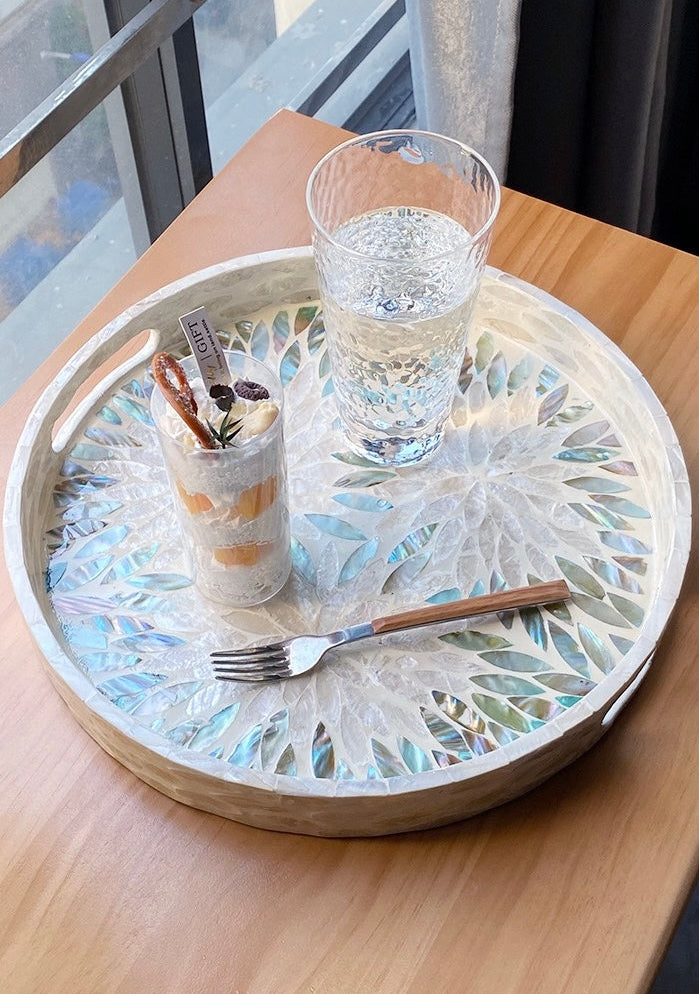 Decorative tray with a glass of water, cup, and utensils on a wooden table.