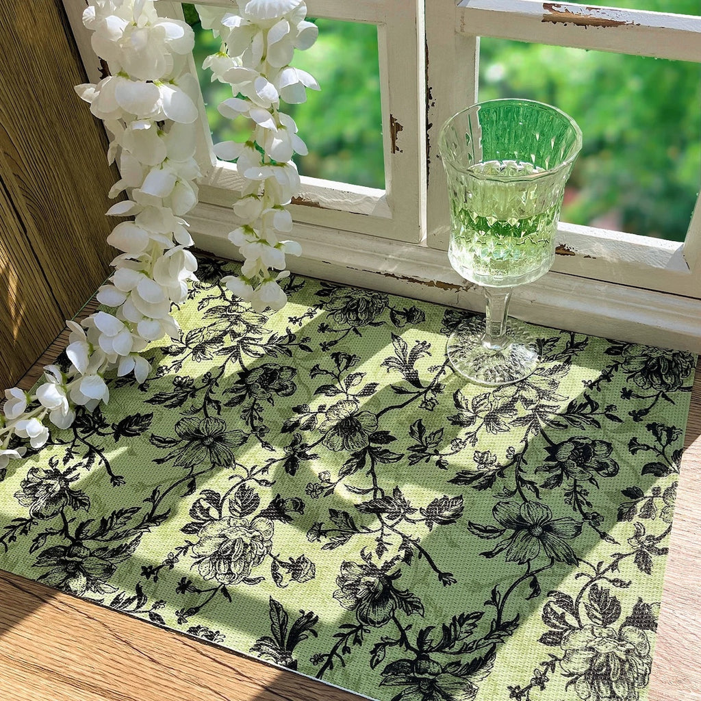Green floral tablecloth with a glass of green liquid on a windowsill with white flowers.