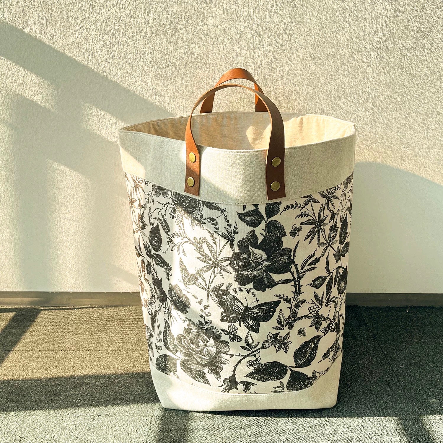 Floral-patterned bag with leather handle on a neutral background